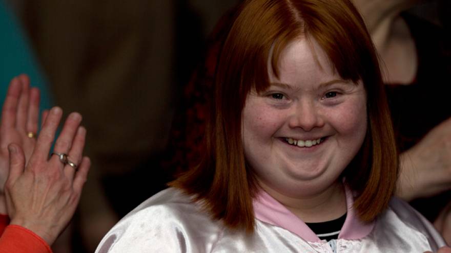Young woman with red hair wearing a pink jacket smiling at the camera