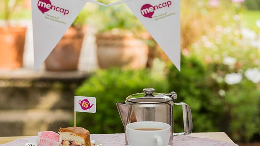 Teacup and cake on a table outside with bunting in background for a tea party