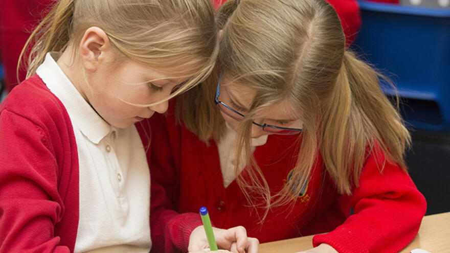 Two schoolchildren sat together working on a craft activity