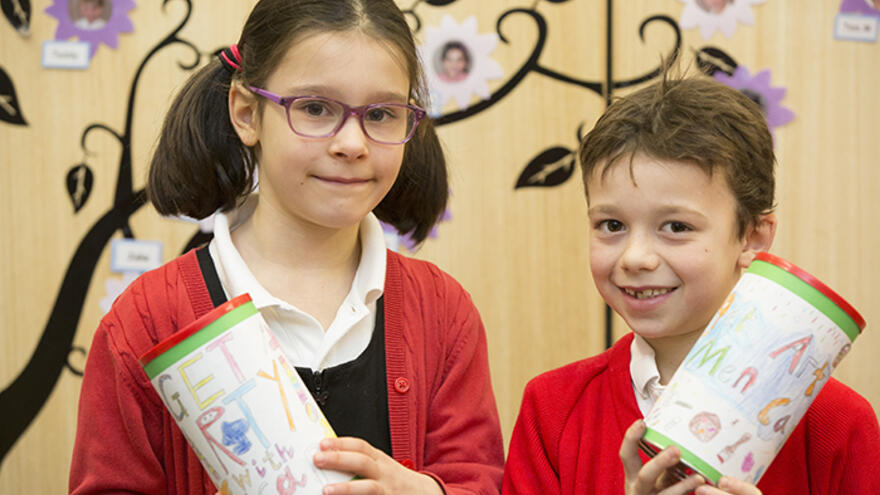 Two children in classroom holding art projects they have made.