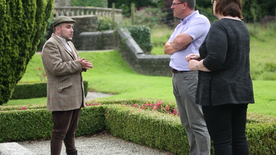 Man stood in National Trust gardens speaking to two other people.