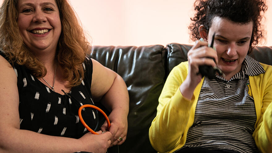 Two women sat together on black sofa.