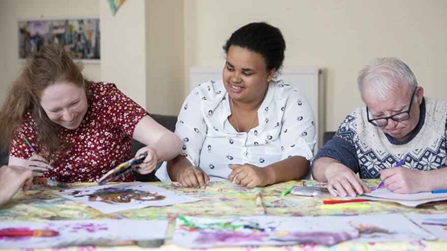 Three people sat at a table doing craft activities