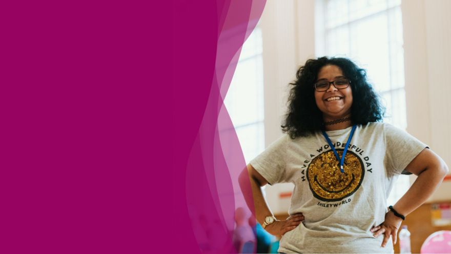An image of a young woman smiling and standing with a power stance. 