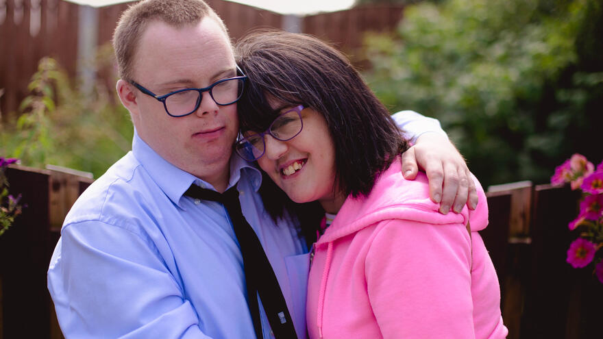 A man with down's syndrome and a woman with a learning disability cuddling.