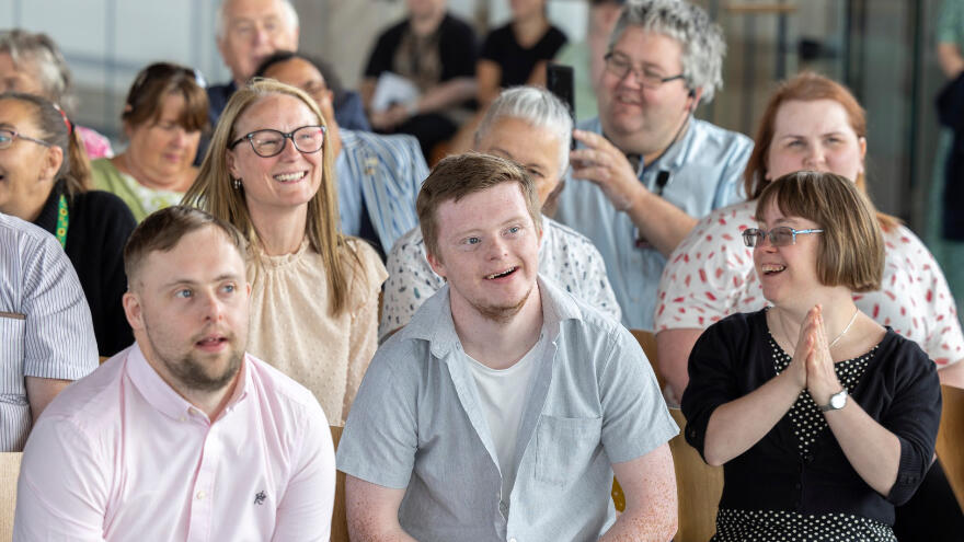 A seated crowd of people with a learning disability laughing.
