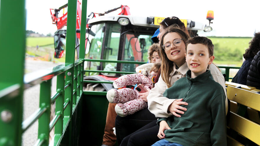 A boy with a learning disability sits on the back trailer of a tractor with a woman who holds him.