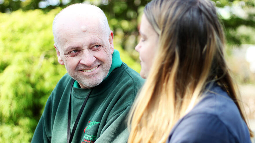 An older man with a learning disability speaks with a member of staff in the grounds of a botanical garden