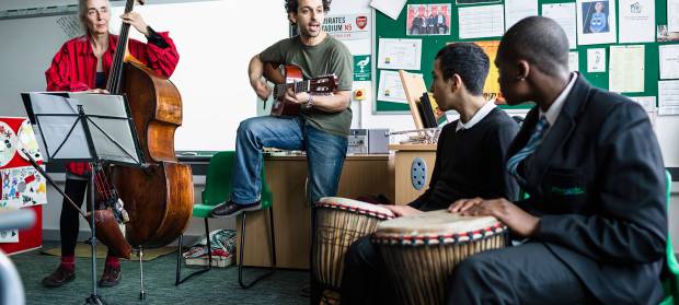Group of four people in classroom, all playing musical instruments.