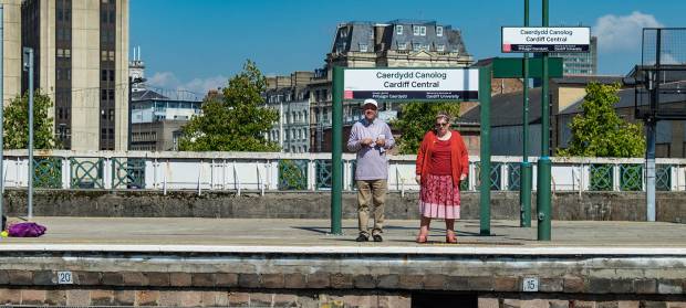 Two people stood underneath sign at a railway station