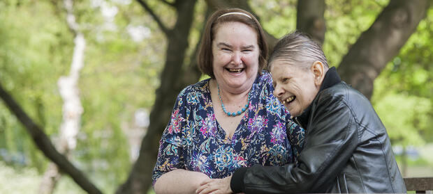 Two women stood together outside in front of a tree, laughing