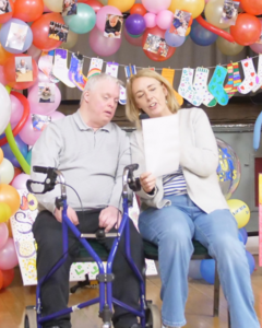 Two people sitting in a community centre with balloons all around them